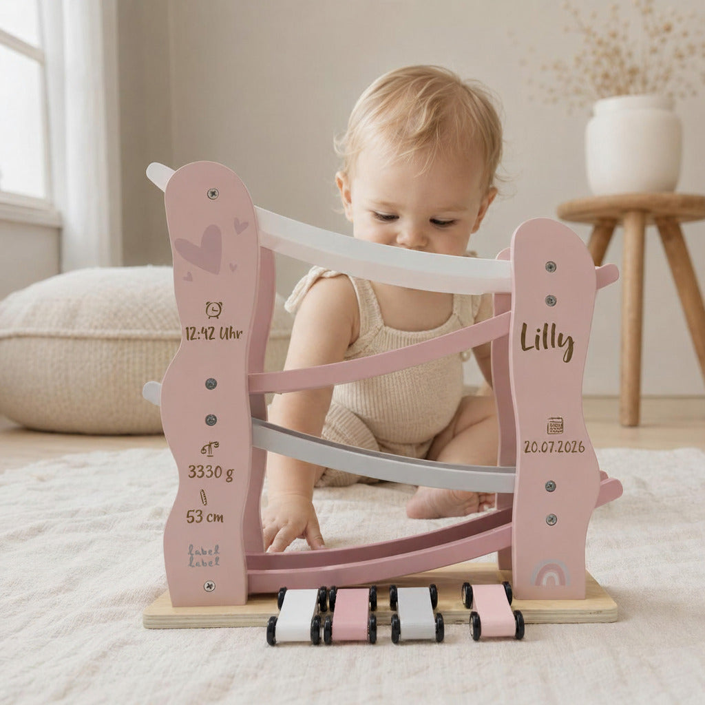 Baby spielt mit einer personalisierten Holz-Rennbahn in Rosa mit vier Autos, Name und Geburtsdaten – besonderes Babygeschenk zur Geburt