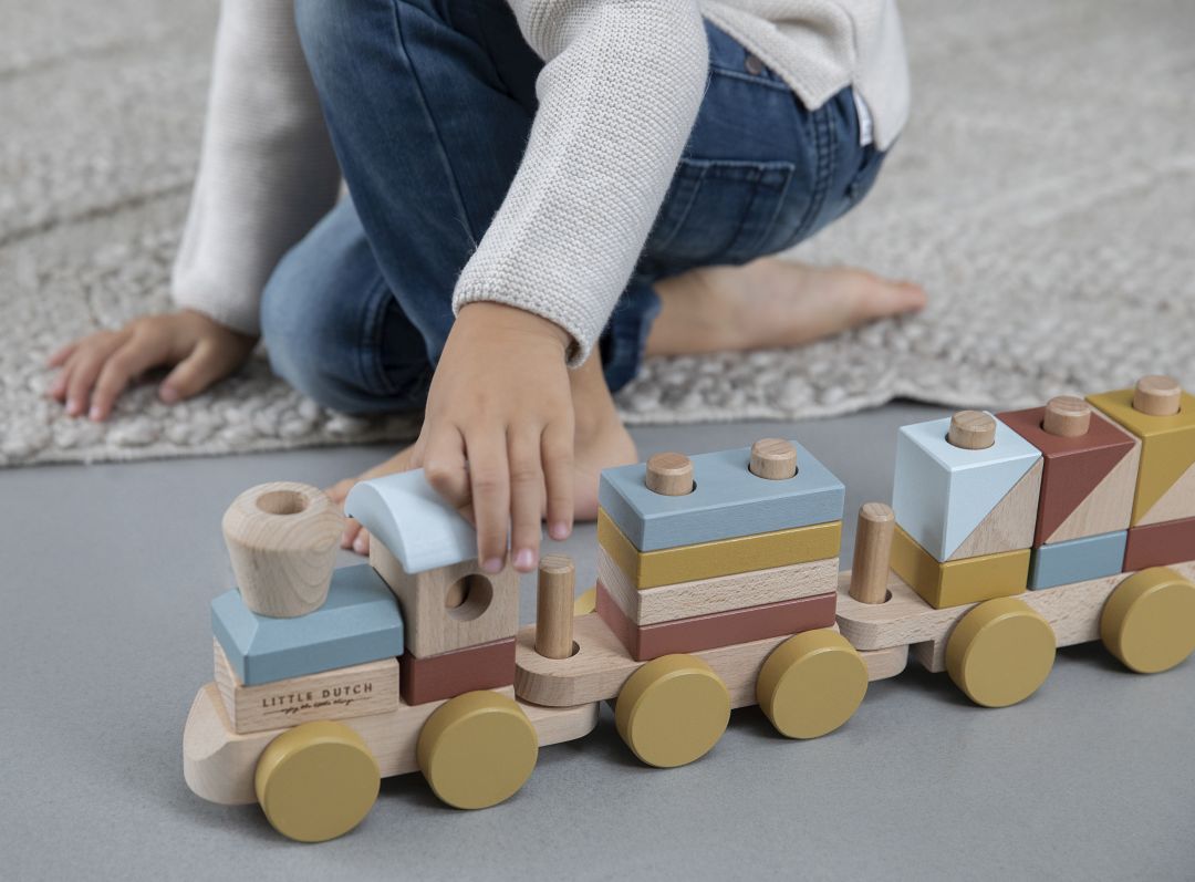 Kind spielt mit dem Holzzug Pure & Nature und steckt farbige Holzbausteine auf Lok und Waggons