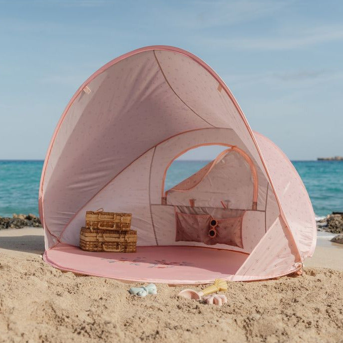 Pinke Strandmuschel für Babys und Kinder am Strand mit Meer im Hintergrund und Spielzeug – UV Schutz Pop Up Strandzelt für sicheren Schatten