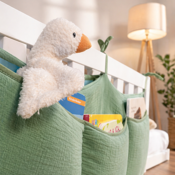 tiSsi Musselin Organizer in Grün mit Büchern und Kuscheltier am weißen Hausbett