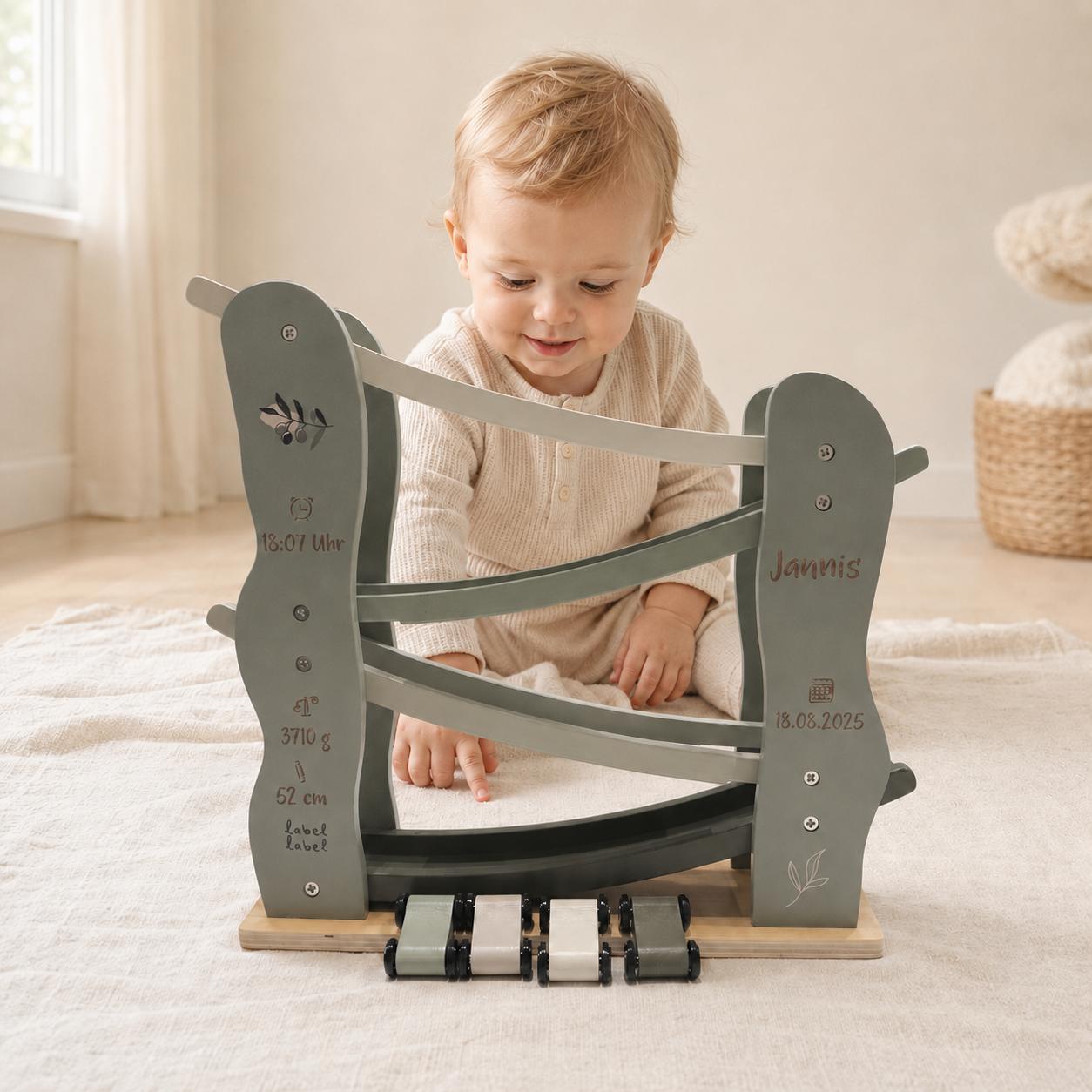 Baby spielt mit einer personalisierten Label Label Holz-Rennbahn in Salbeigrün mit vier Autos, Name und Geburtsdaten – besonderes Babygeschenk zur Geburt.