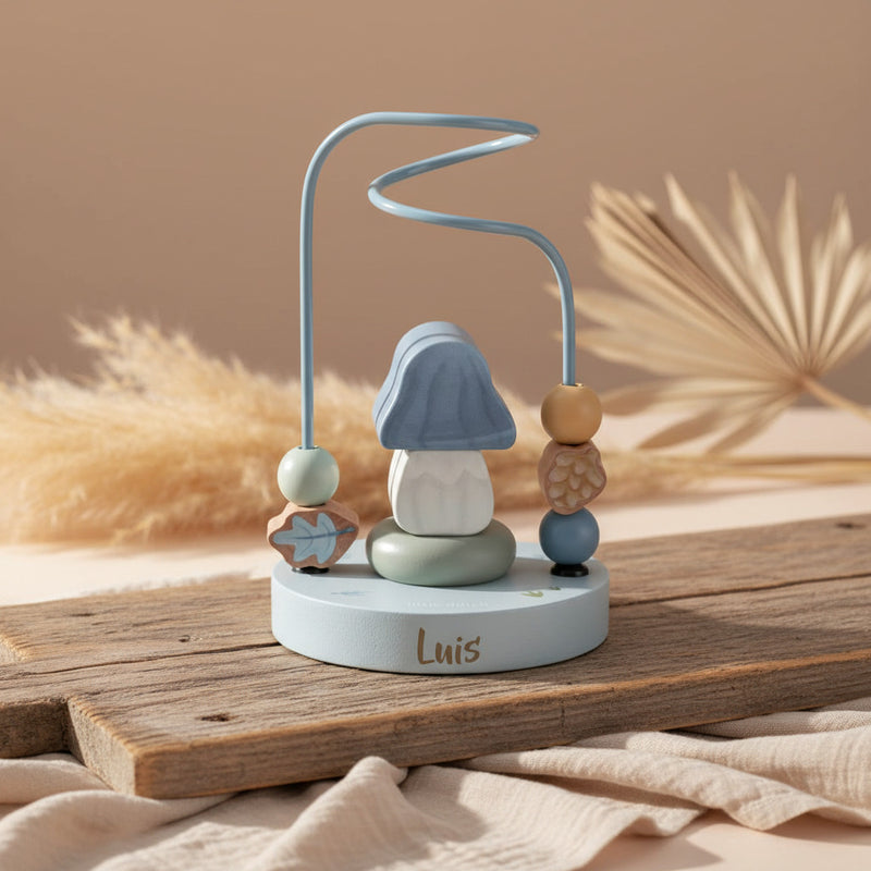 Personalisierte Little Dutch Aktivitätsspirale Forest Friends aus Holz mit Namen Luis vor getrockneten Palmblättern.
